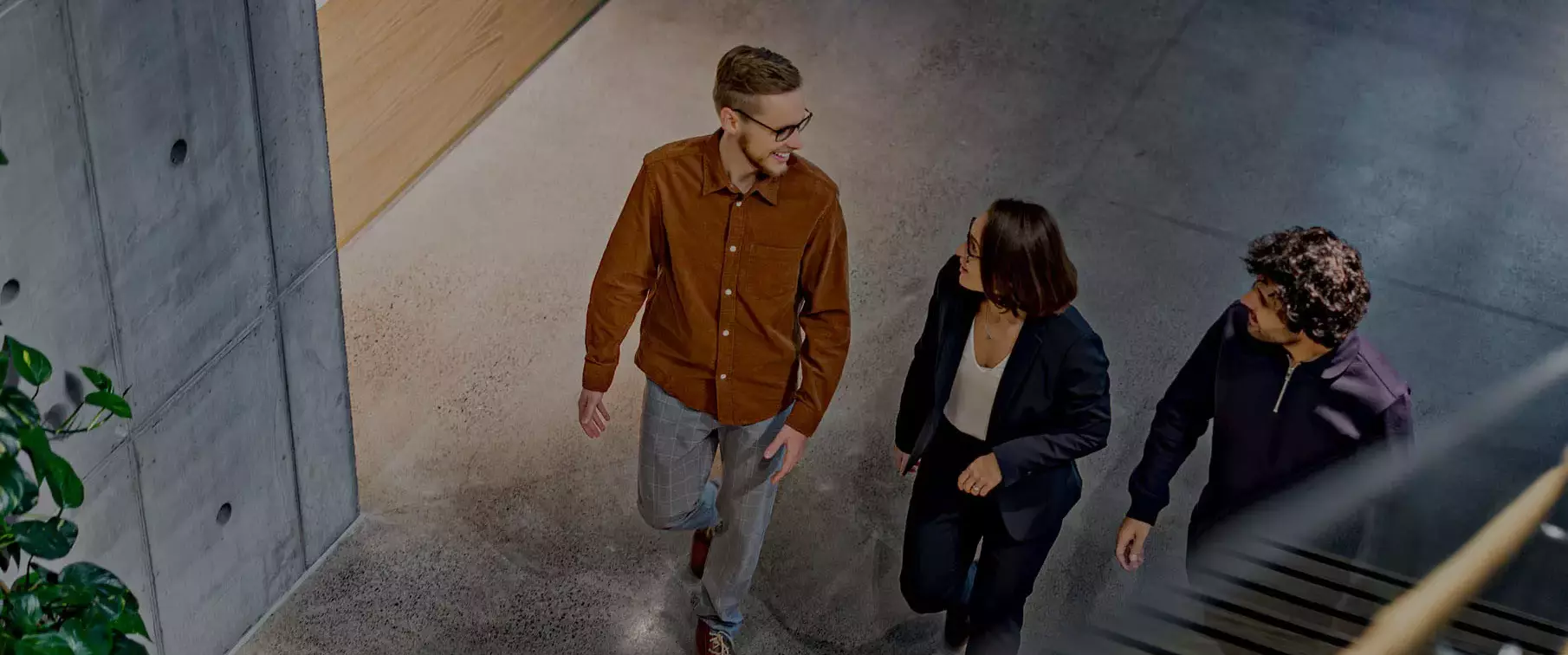 Kolme iloista ihmistä katsoo toisiaan ja kävelee toimistorakennuksen sisällä